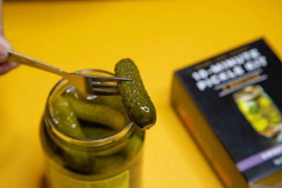 Pickling perfection cucumber on a fork with Johnny and Pearl pickling spice box in the background